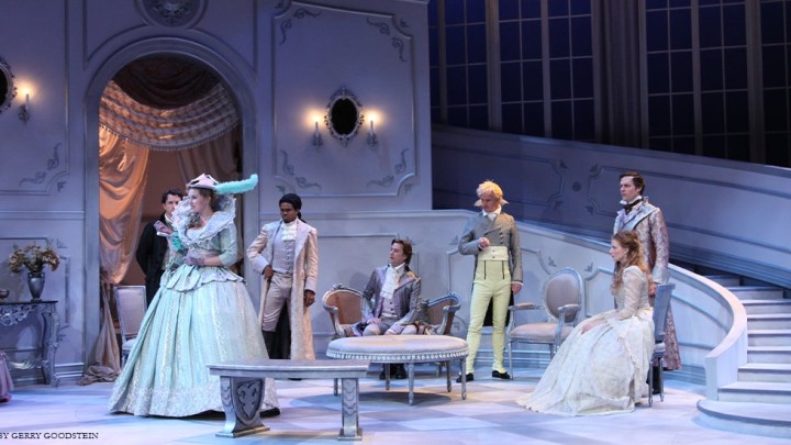 Seven actors on a white stage with a grand staircase wearing period clothing.
