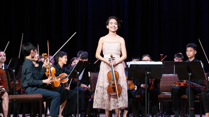 A female violinist standing in front of an orchestra