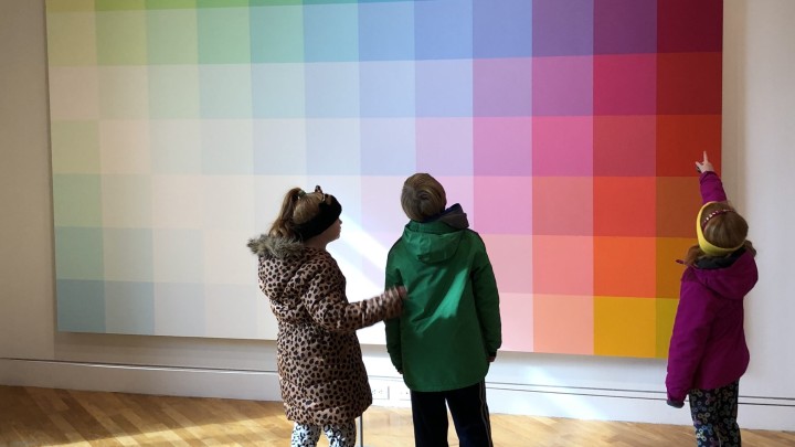 Three people stand in front of a color gradient mosaic art piece at the Visual Arts Center of New Jersey.
