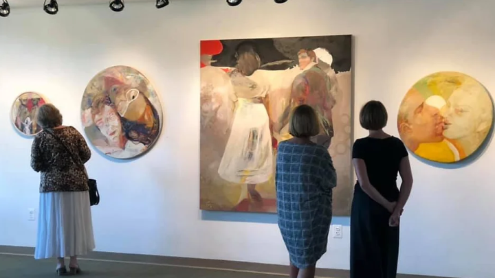 A group of people looking at paintings in an art gallery.