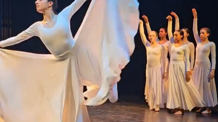 A group of dancers in white dresses on stage
