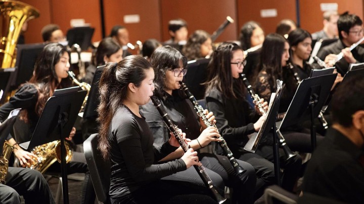 Children in an orchestra, wearing all black, playing their instruments.