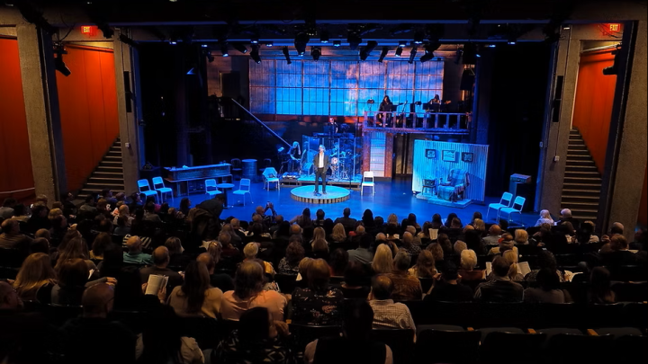 A theater stage with an audience of people seated in rows, attentively watching a performance.